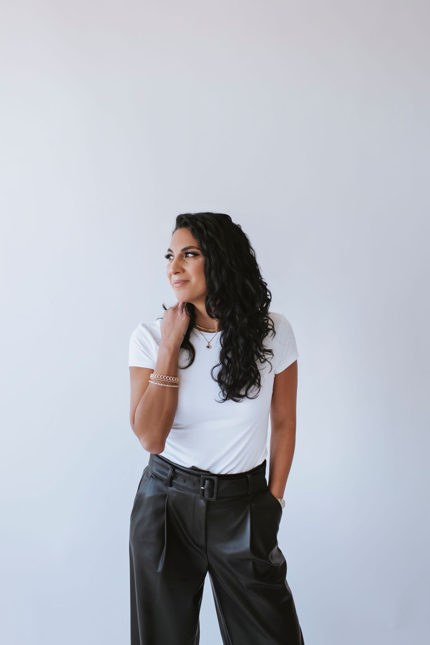 A woman poses looking to the side in front of a white wall. She is wearing black and white and looks modern and professional.