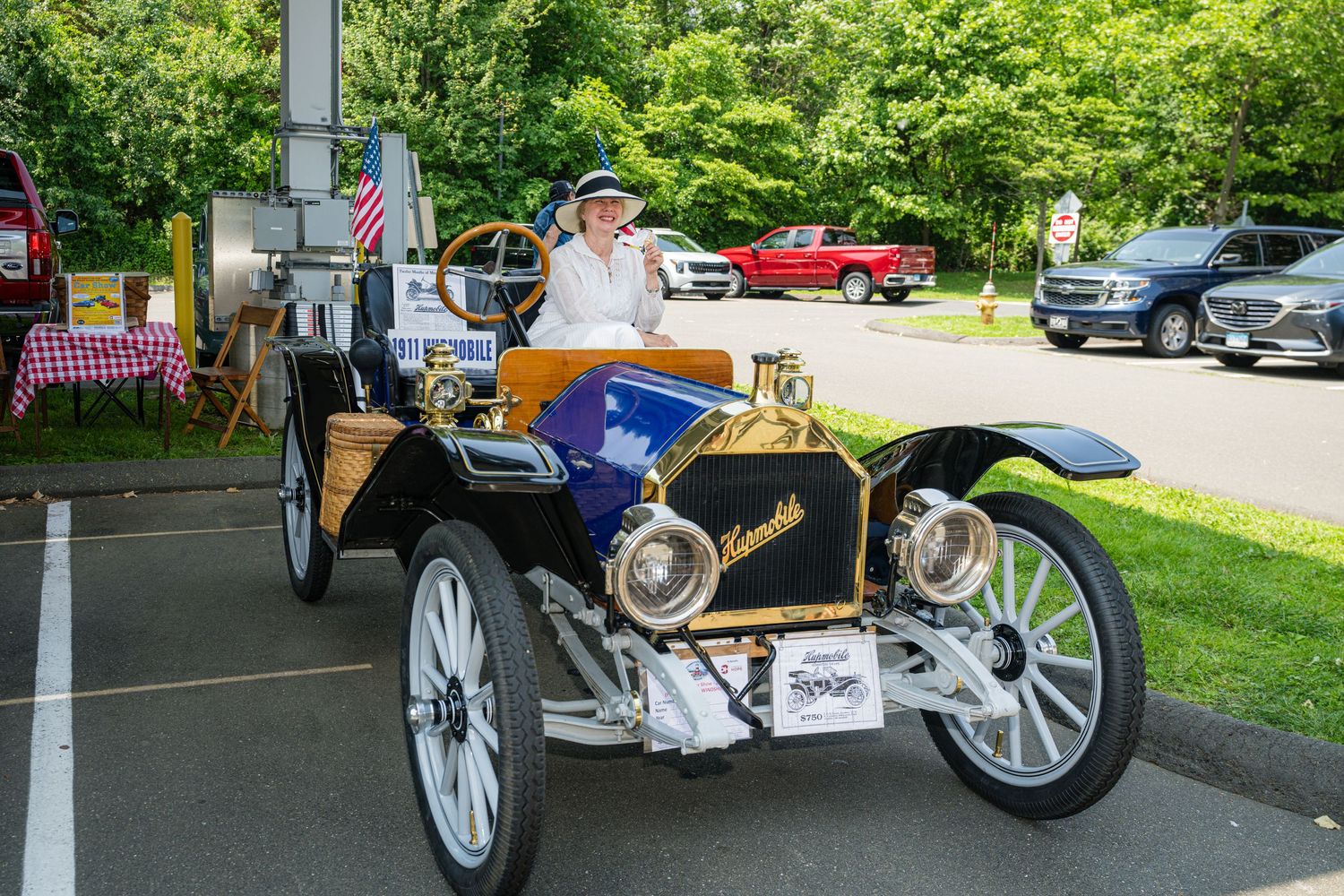 Vintage black automobile with white wooden spoke wheels displayed at outdoor car show with trees in background.