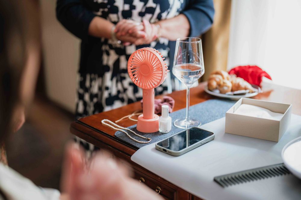 Pink handheld fan and wine glass on wooden table during wedding preparations.