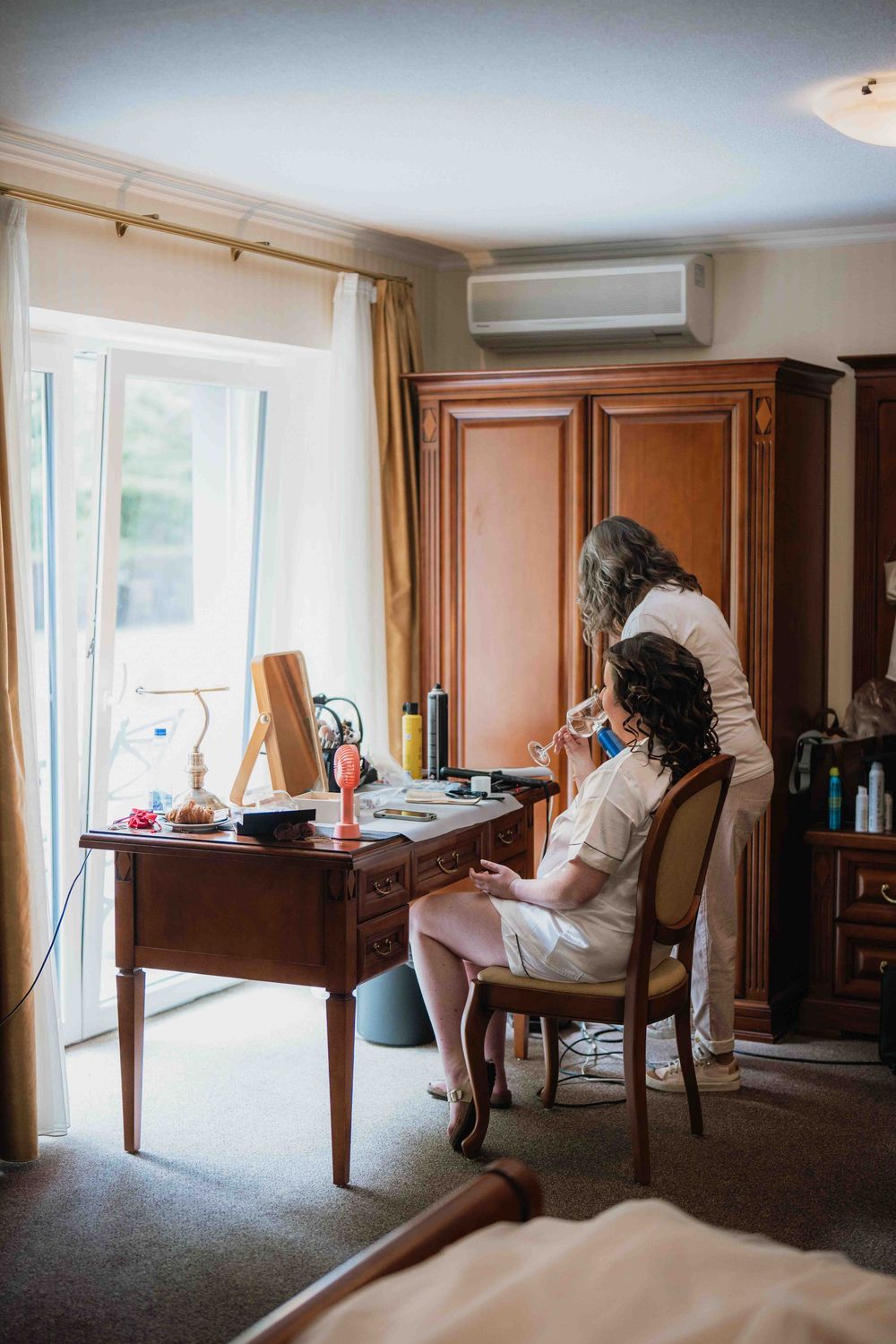 Sunlit hotel room with wooden desk and chair near a large window.