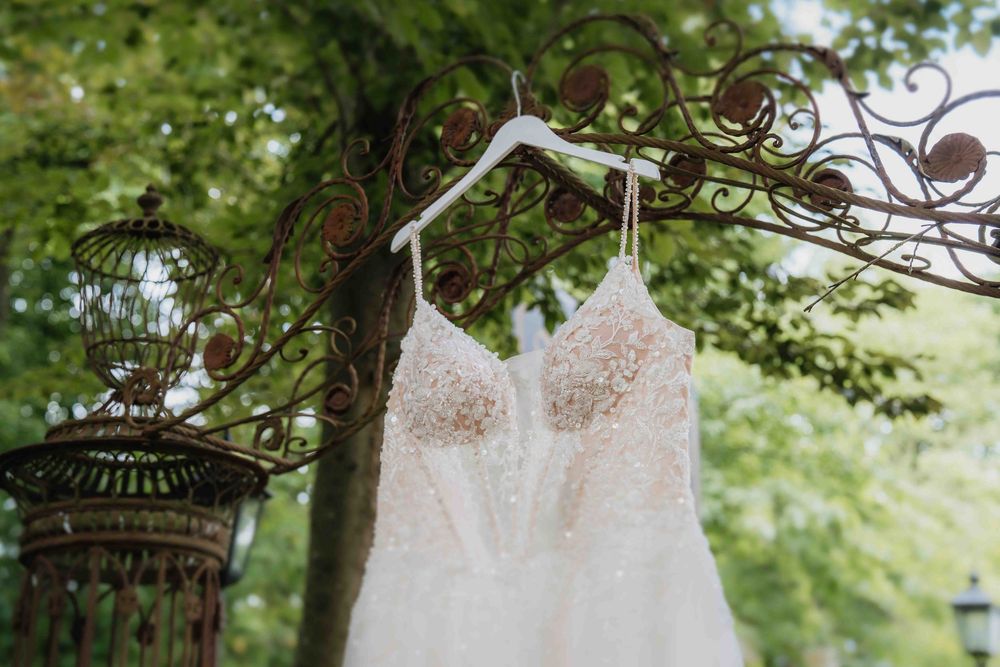 White lace wedding dress hanging from a tree branch with green foliage in background.