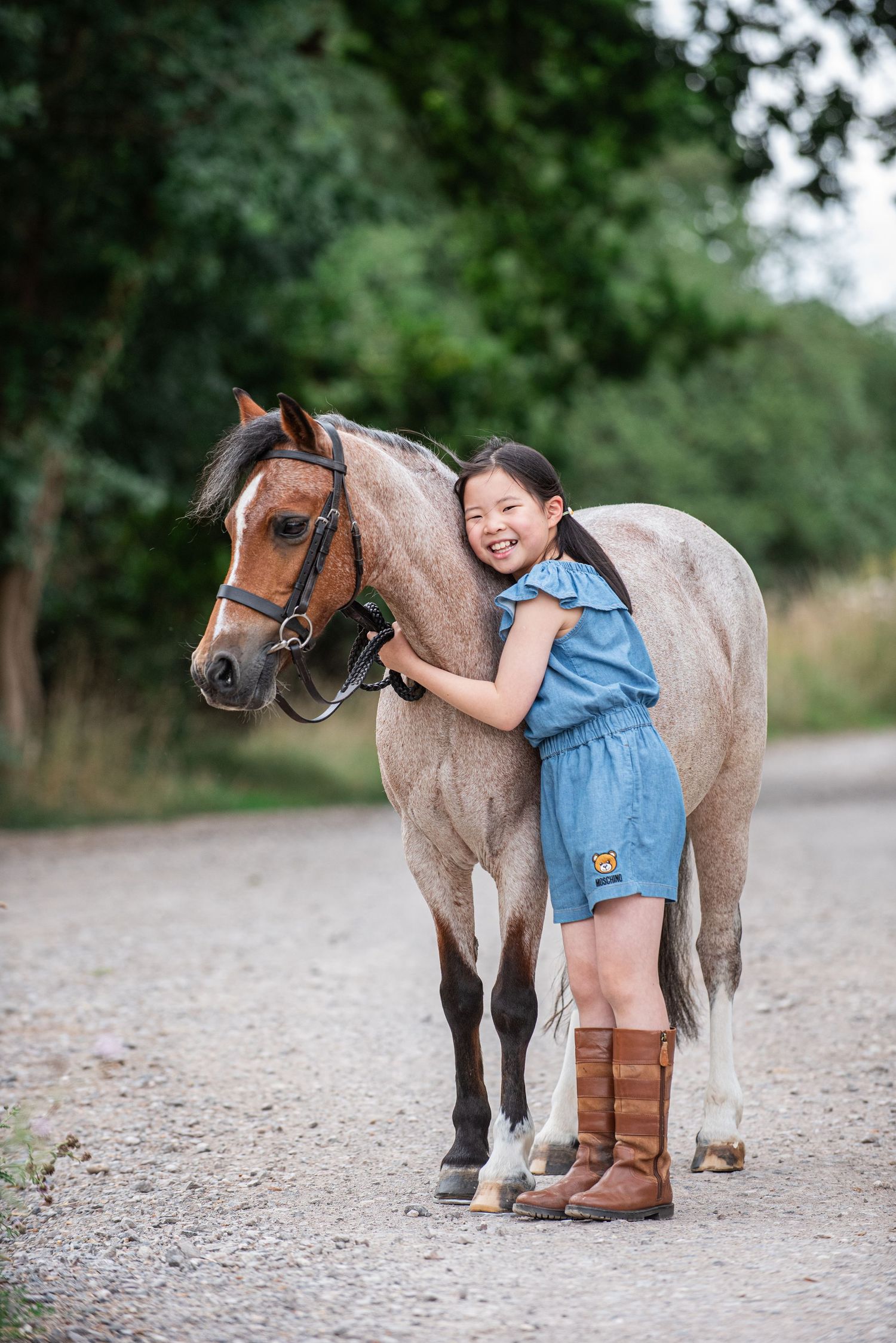 Olivia Mu smiling cuddling her strawberry roan pony, Pickle wearing a Moschino playsuit and todpur country boots