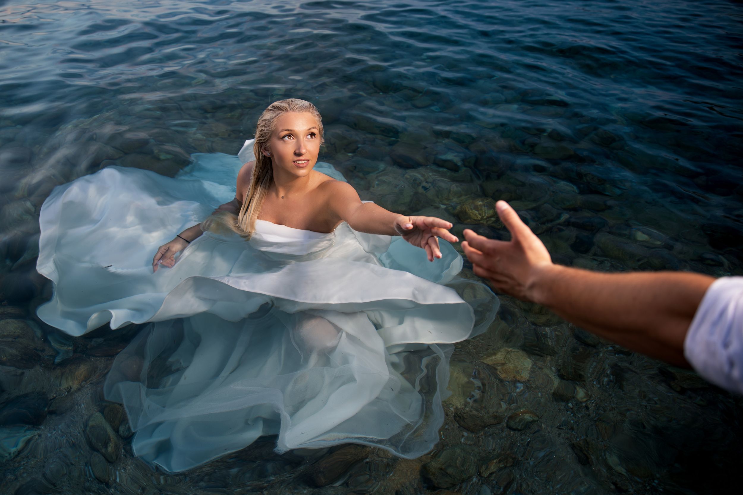 Romantic water photoshoot with flowing white dress in dark lake waters.