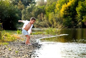 Person skipping stones across a tranquil river surrounded by lush greenery.