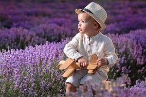 Child wearing a sunhat sitting among vibrant purple lavender fields at sunset.