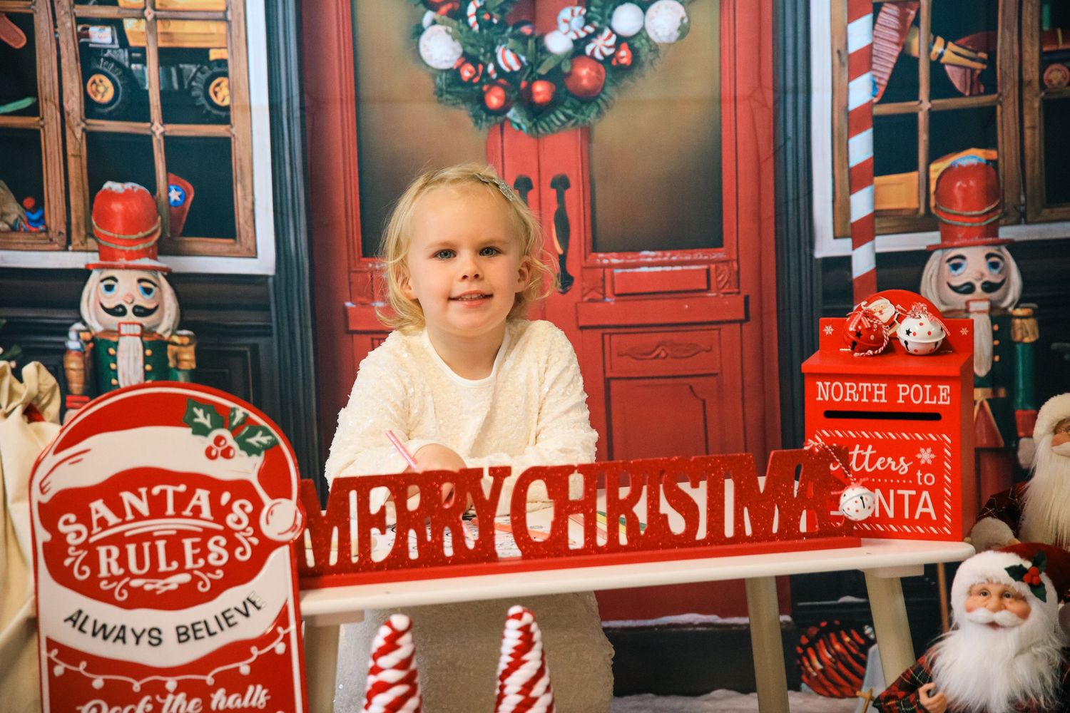 A holiday scene with a red door, Christmas decor, and a festive Merry Christmas sign surrounded by decorative elements.