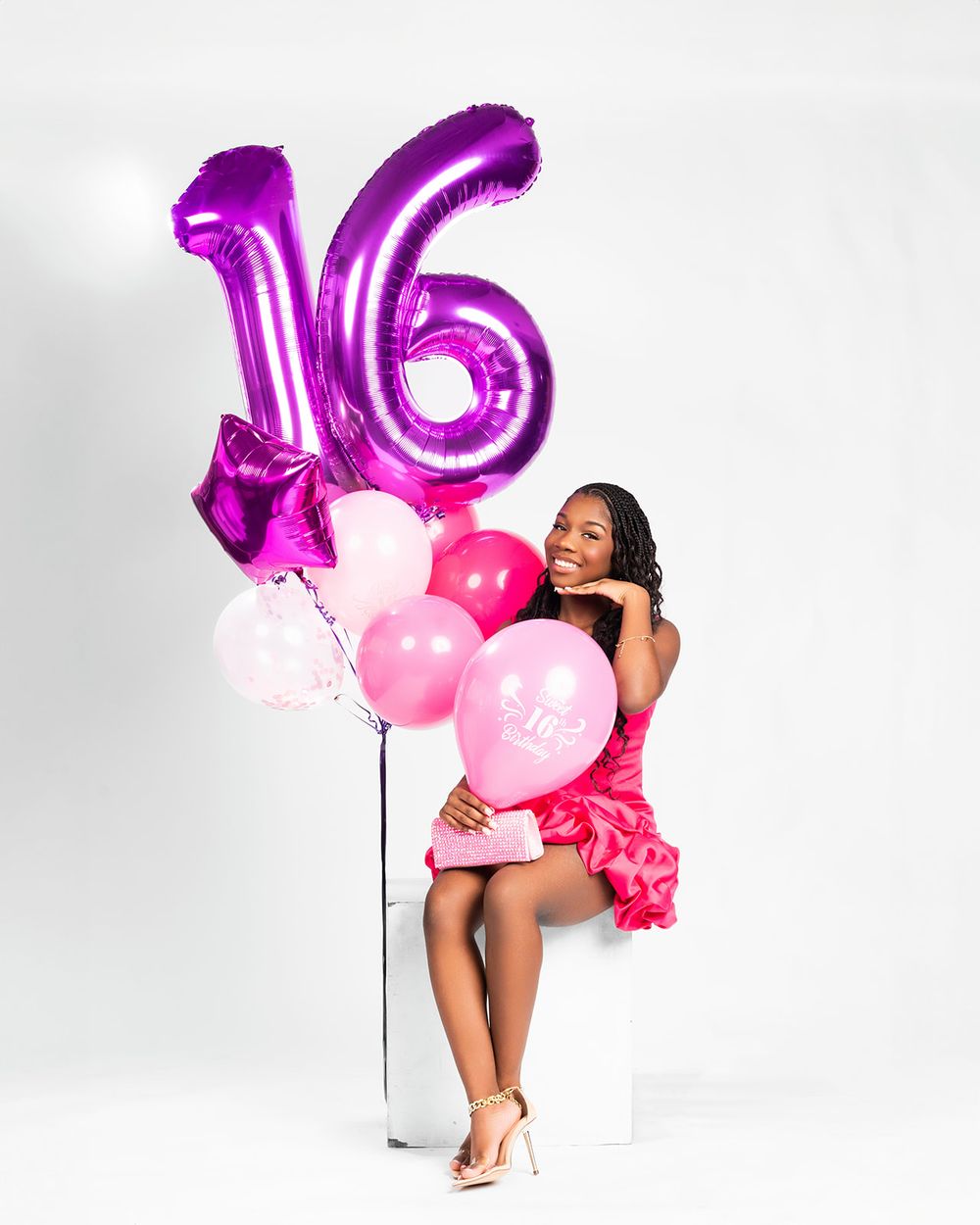 Sweet sixteen celebration photo with model posing next to purple number balloons and pink decorations.