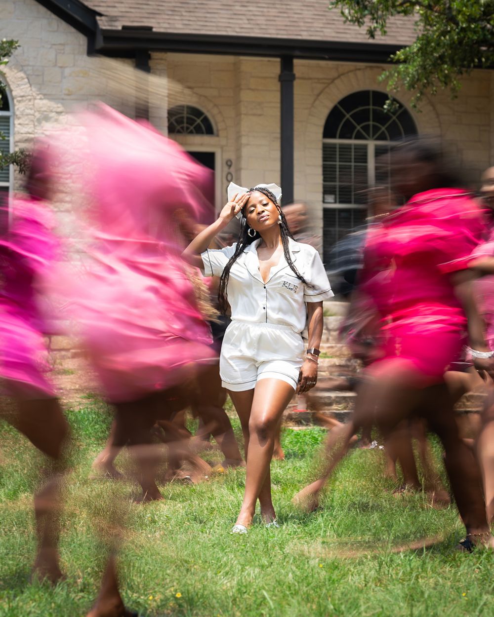 A figure in white poses while others in pink create motion blur in an outdoor photoshoot.