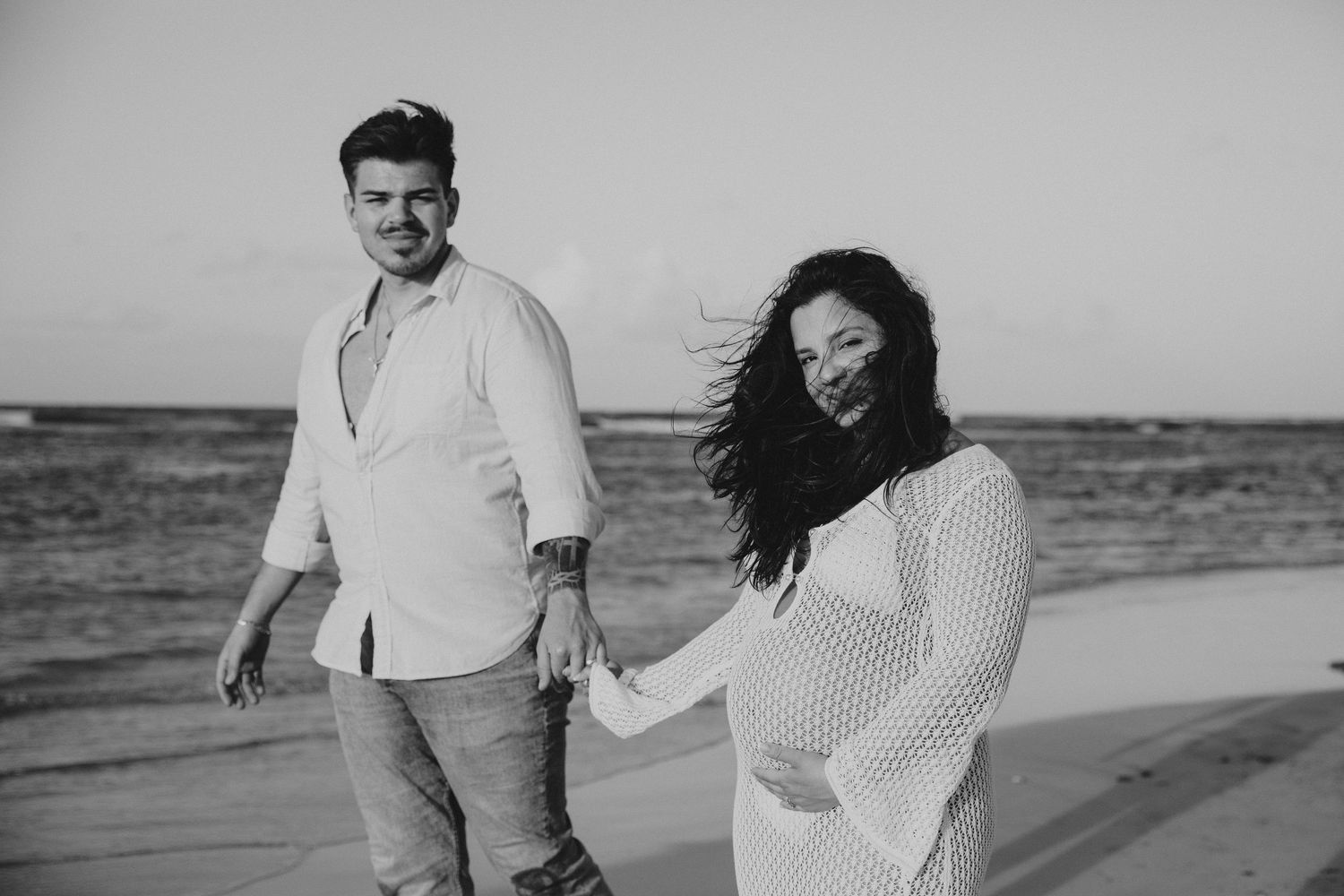 Natural beach photoshoot with couple in white clothing against ocean backdrop.