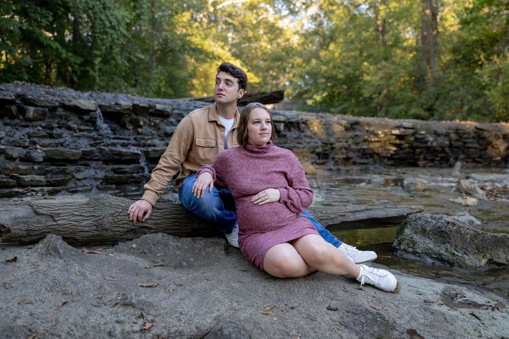 A couple sits together on rocky terrain during a golden hour photoshoot in nature.
