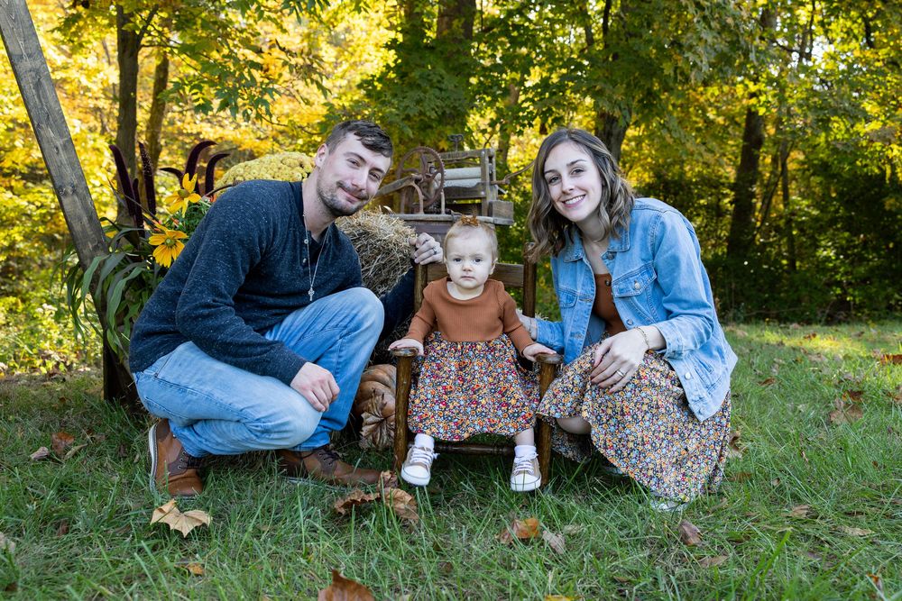 Family enjoying autumn weather together sitting on grass with golden fall foliage in background.