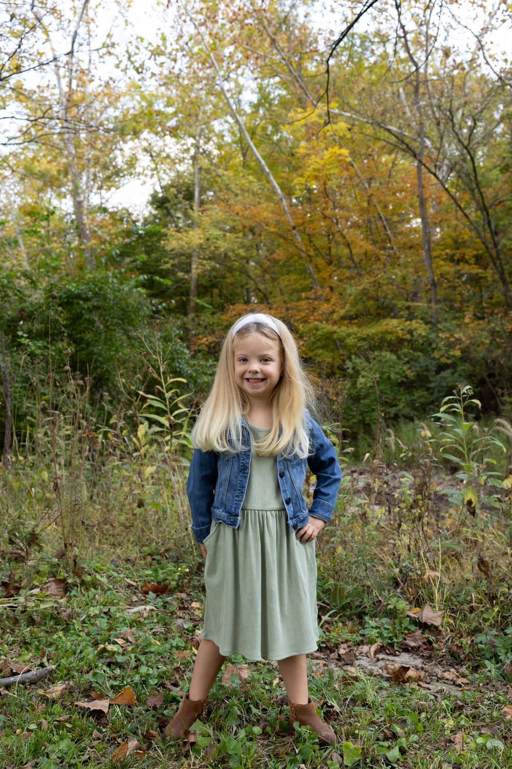 Young girl in denim jacket and mint dress playing in autumn woods.