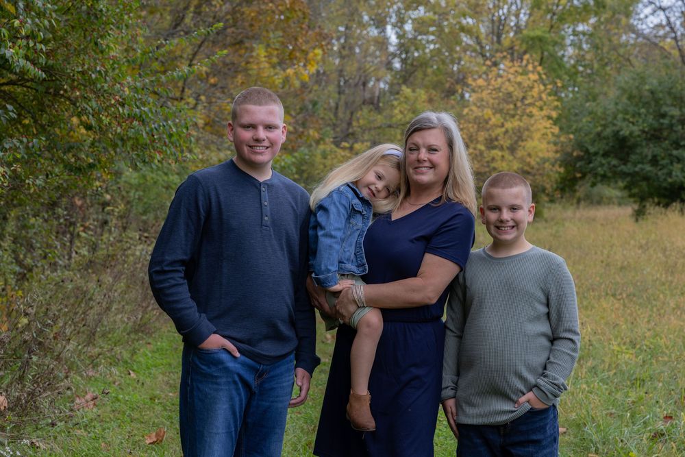 Family members standing together in casual attire against autumn forest backdrop.