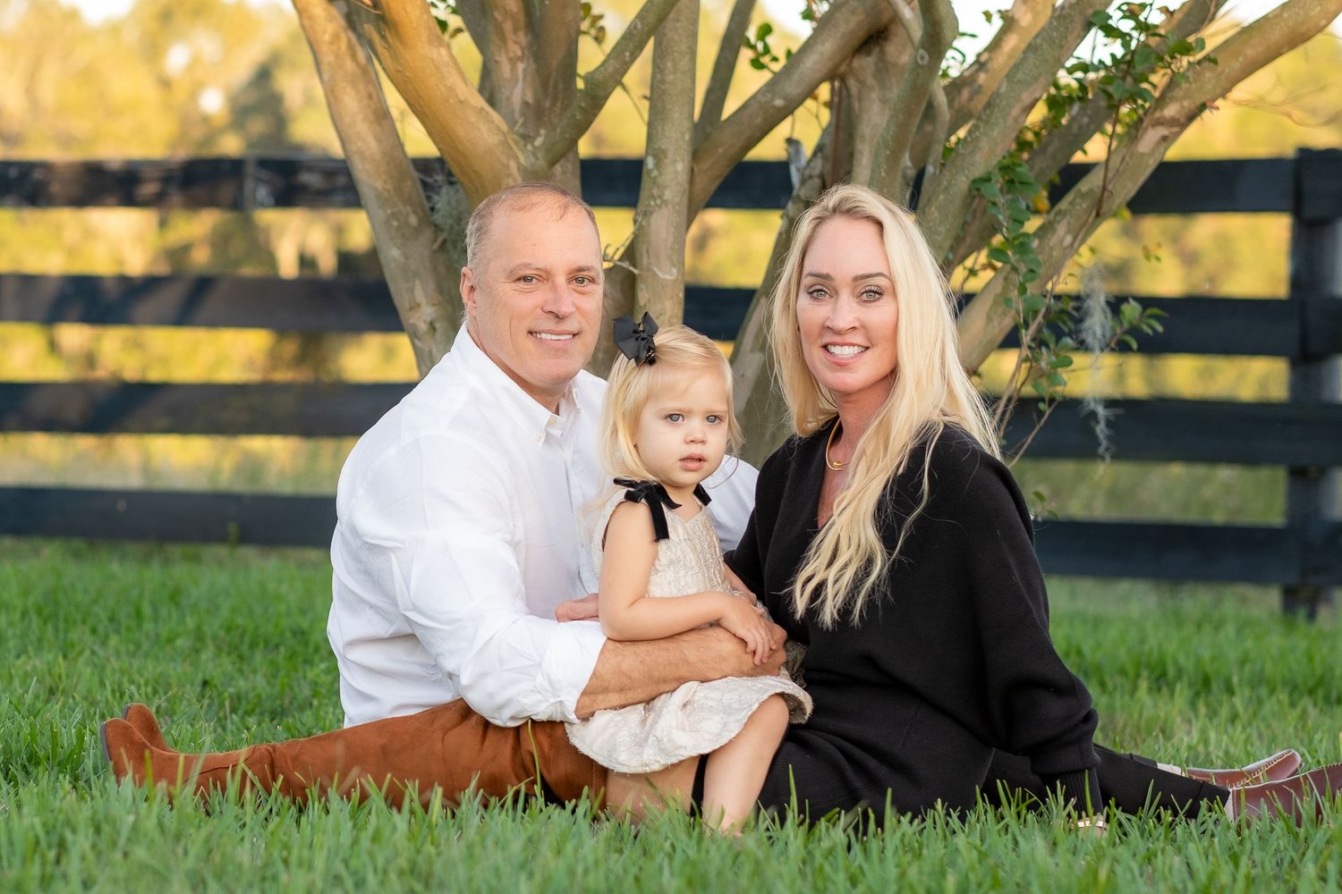 A relaxed family portrait in front of a striped black and yellow fence with a tree in the background.