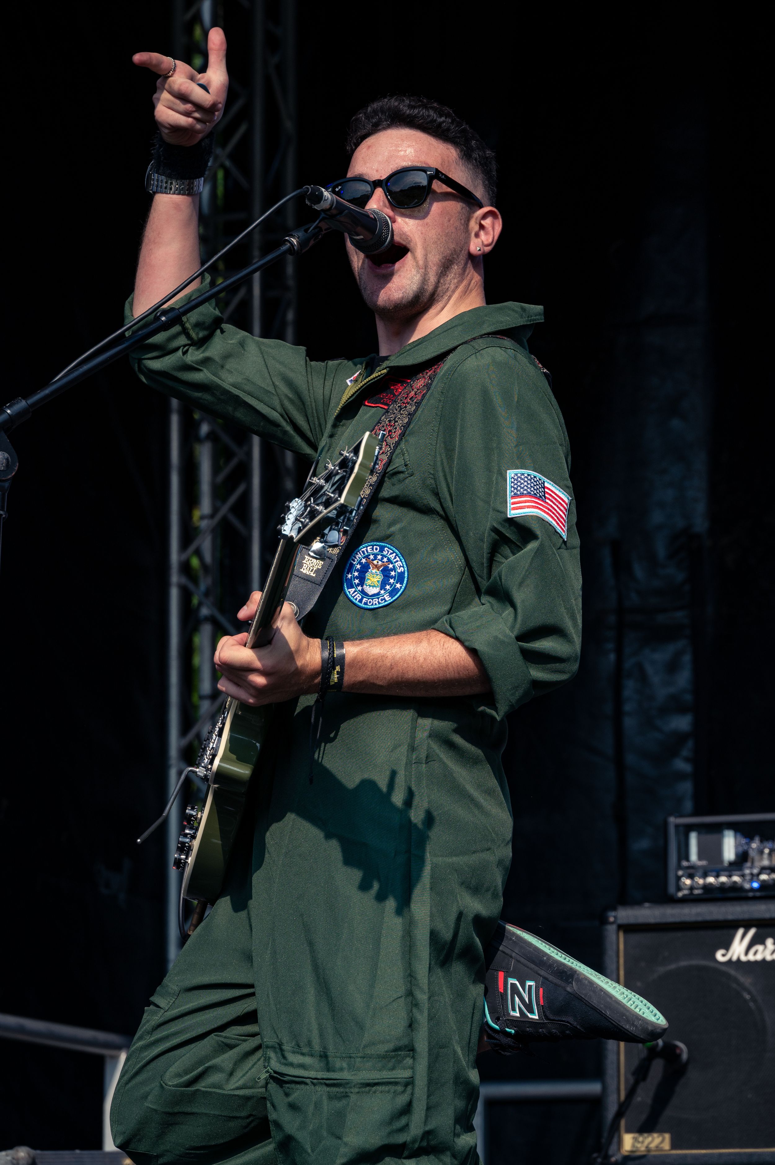 Rock musician in military-style uniform performs with guitar and microphone on concert stage.