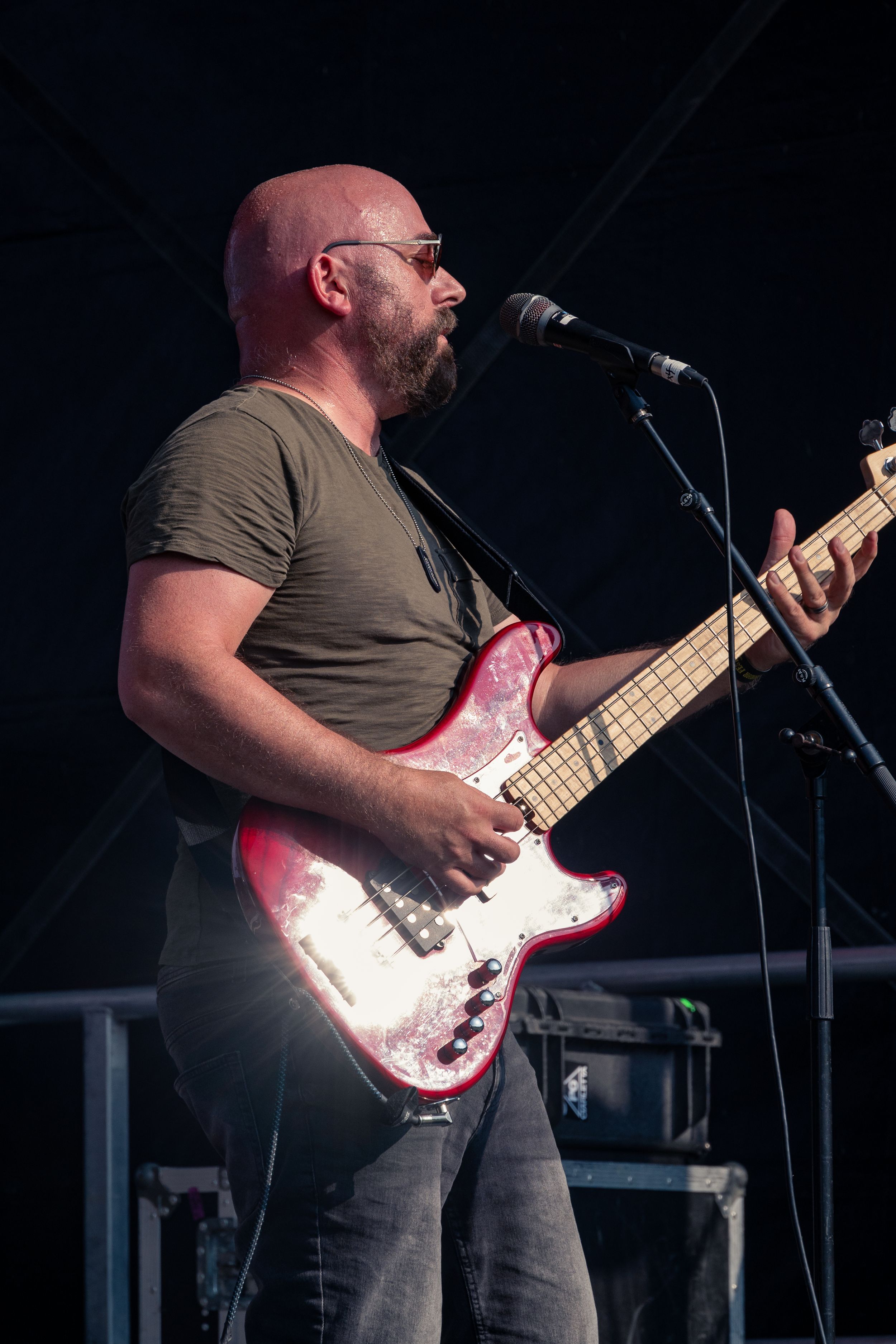 Musician plays pink bass guitar while singing during outdoor performance.