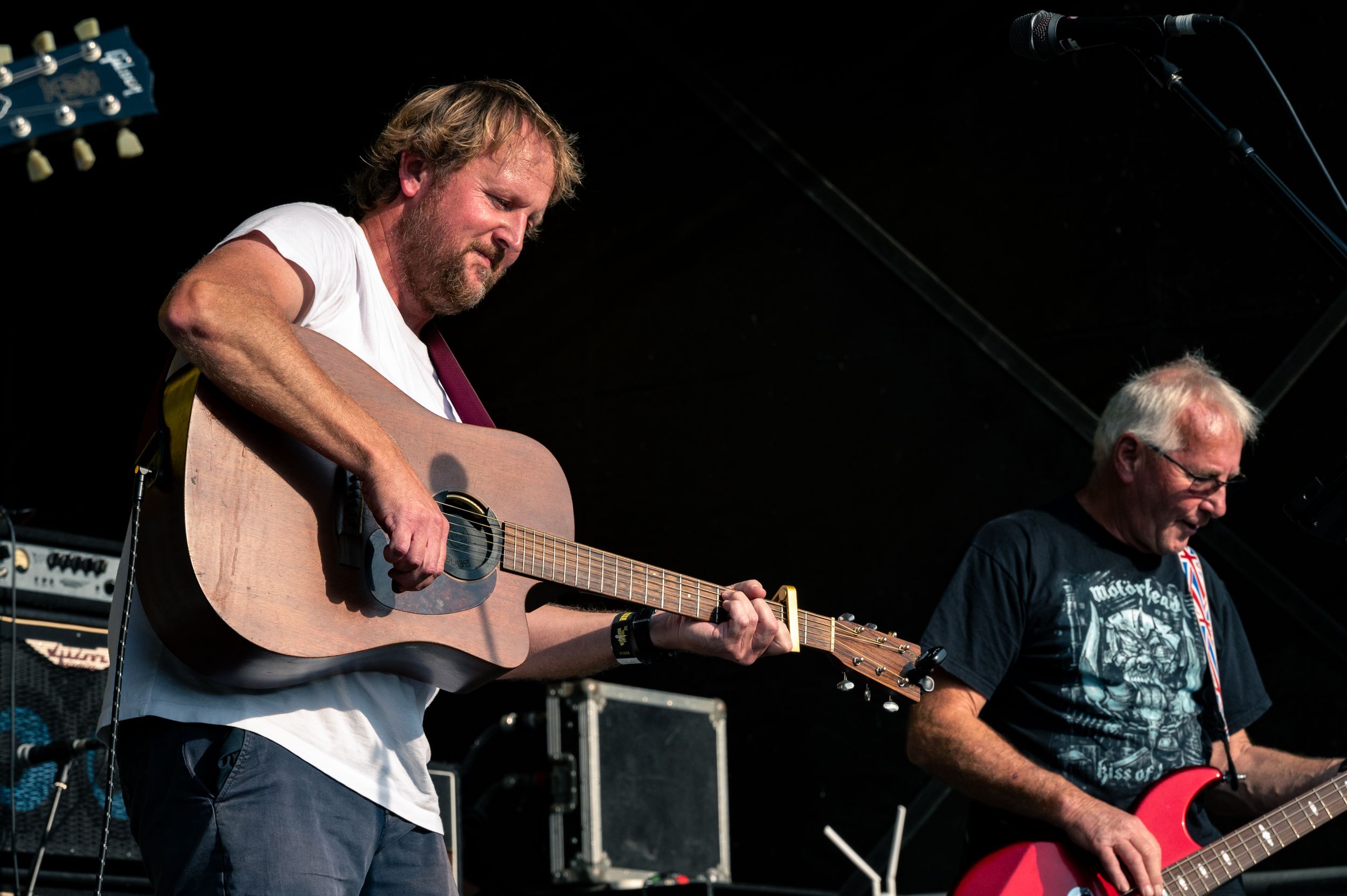Musicians perform energetically on outdoor festival stage with guitars.