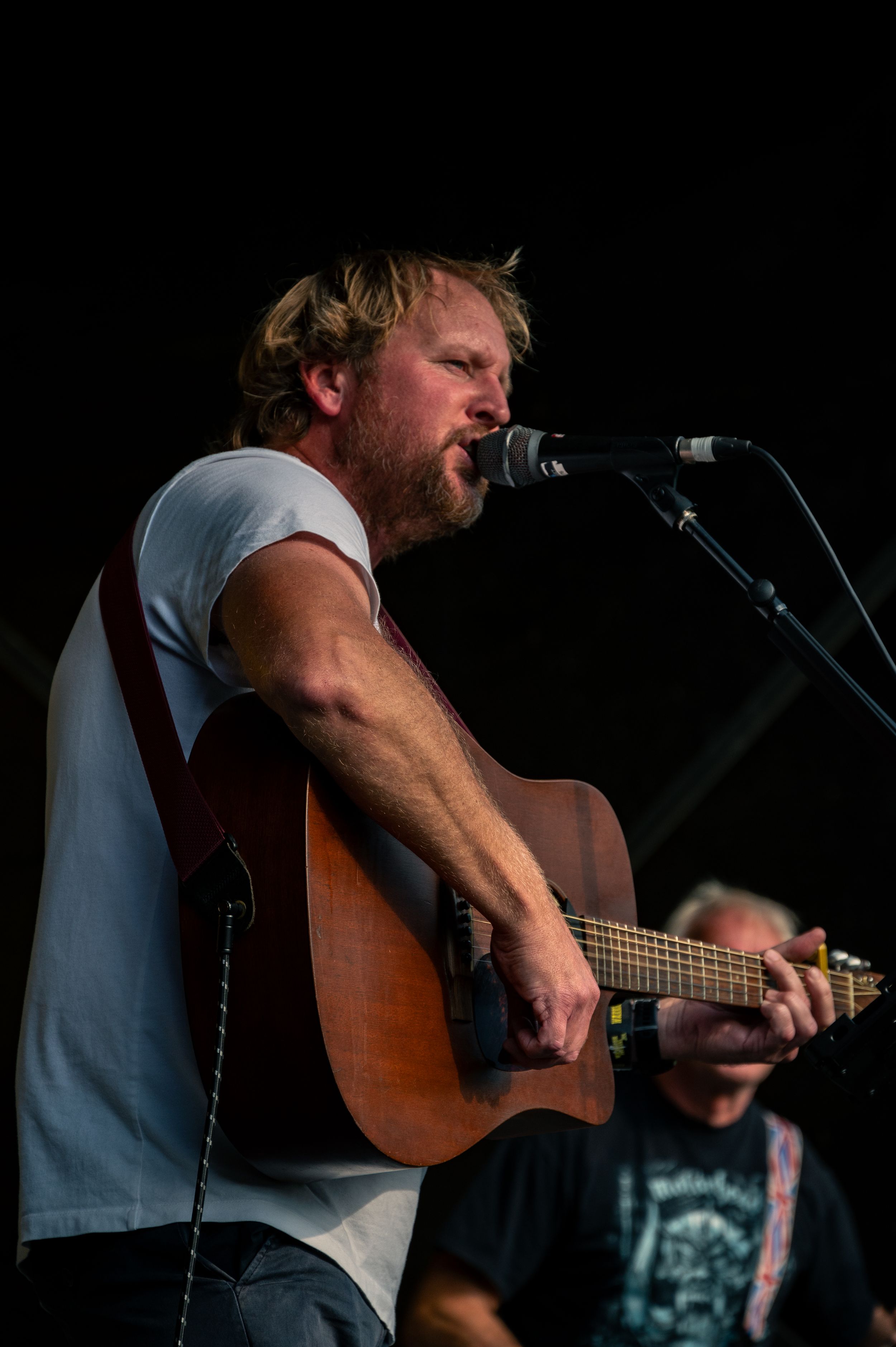 Vocalist performs passionately with acoustic guitar during outdoor concert.