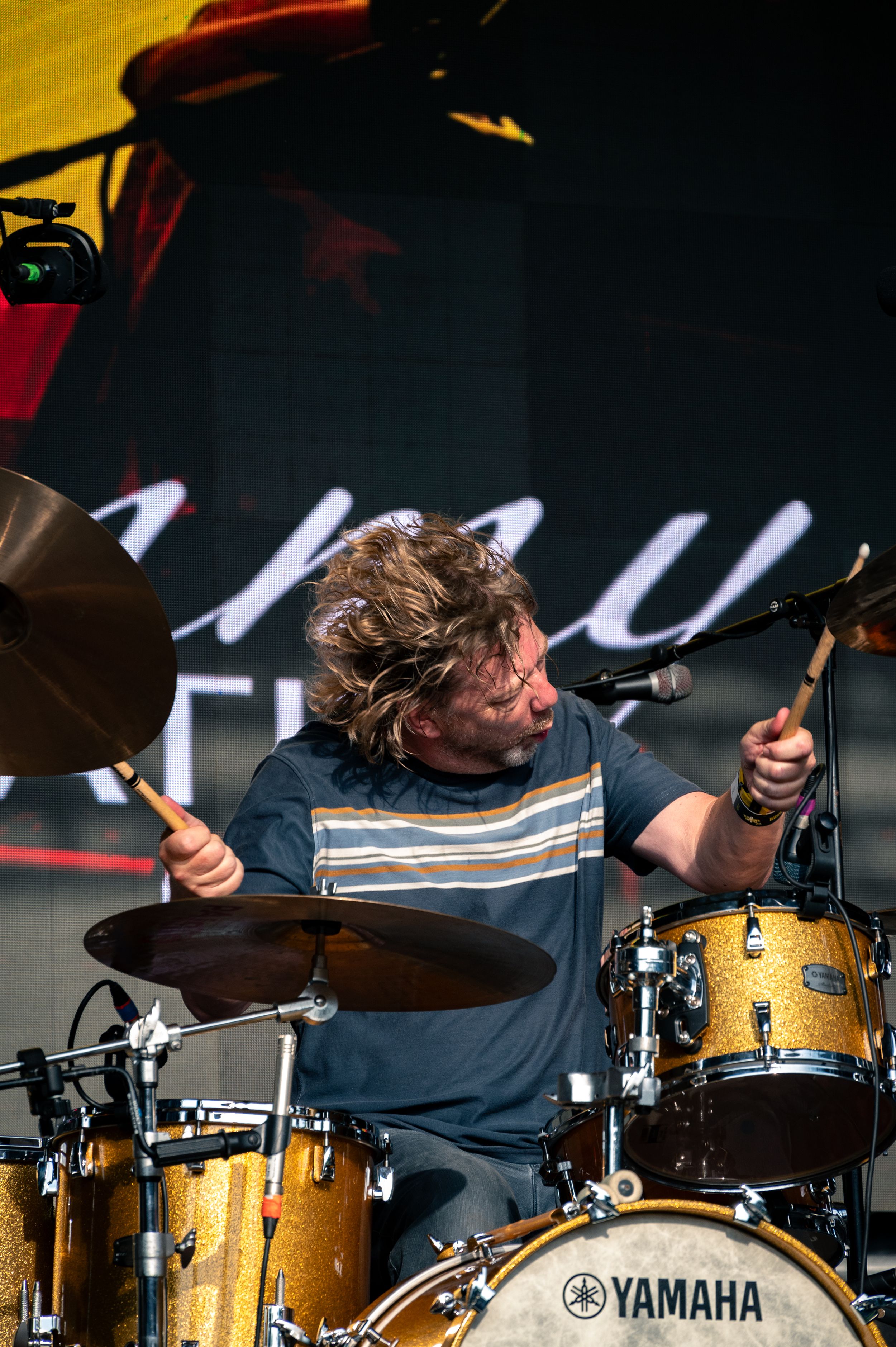 Drummer plays Yamaha kit with intense expression during outdoor performance.