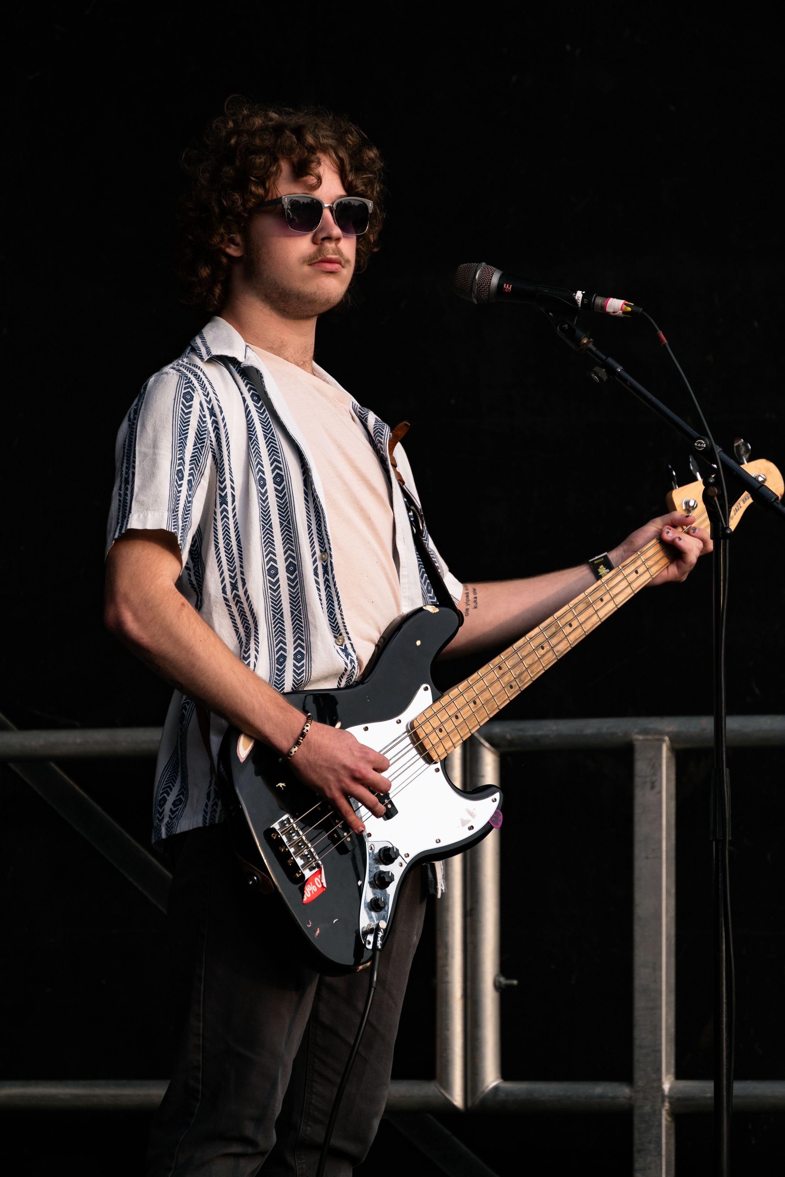 Bass player in striped shirt performs on stage with black and white bass guitar.