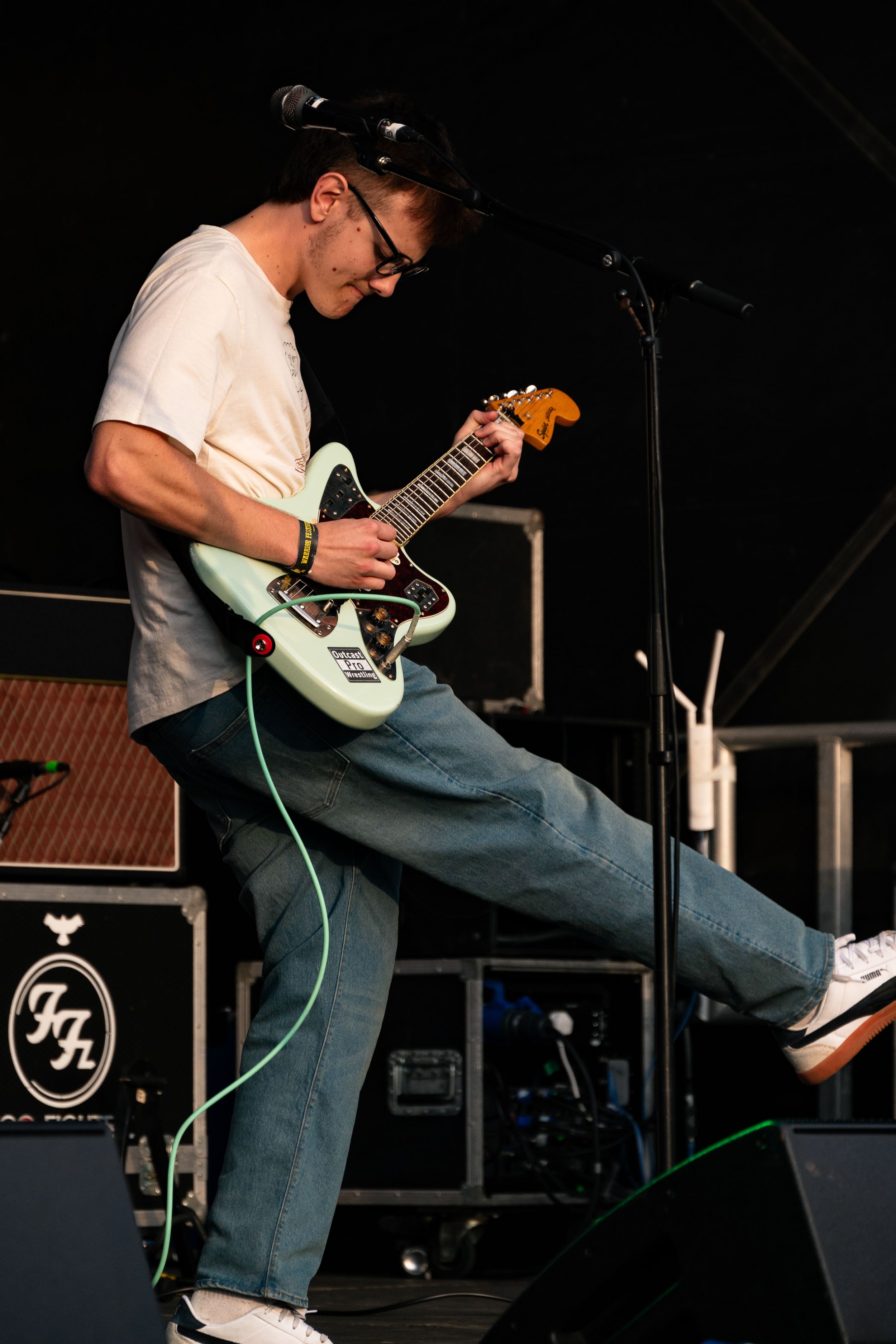 Guitarist in casual wear plays mint colored electric guitar while performing energetic stage move.