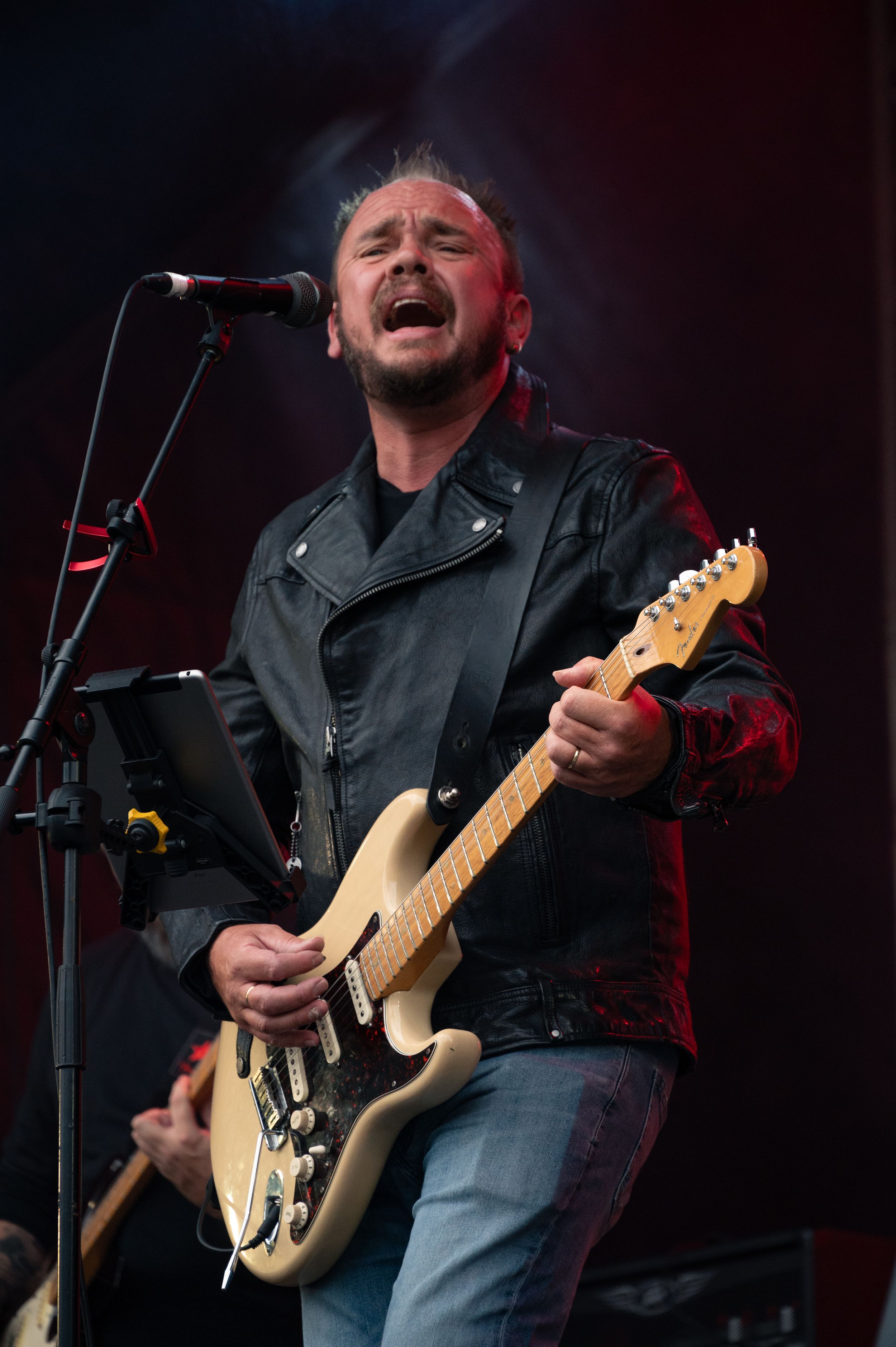 Musician performs passionately on stage with a cream-colored electric guitar while singing into a microphone.