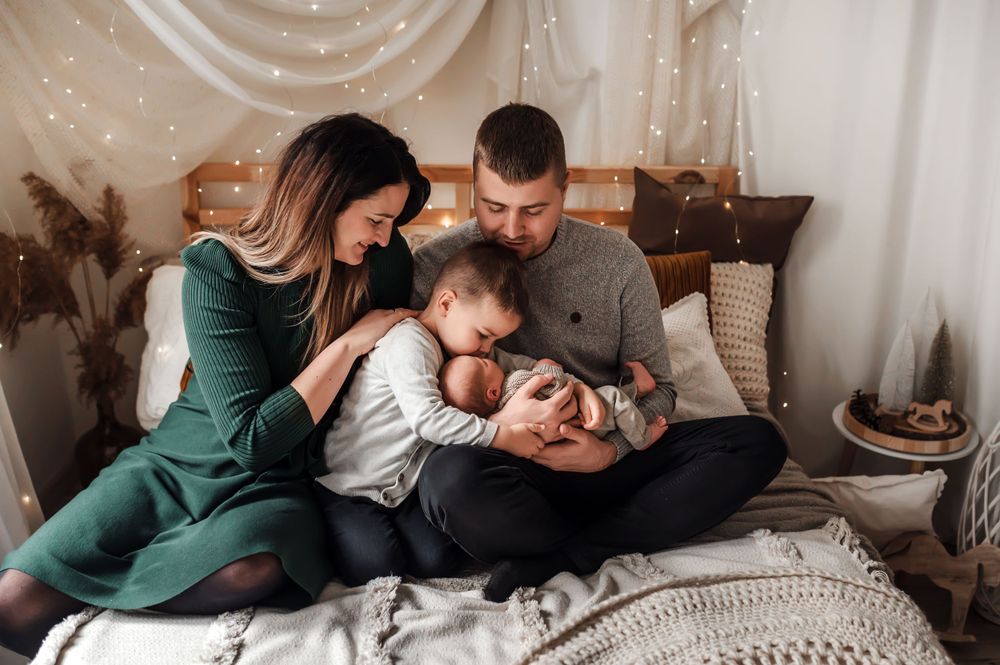 Family enjoying tender moments together on bed with string lights and decorative pillows.