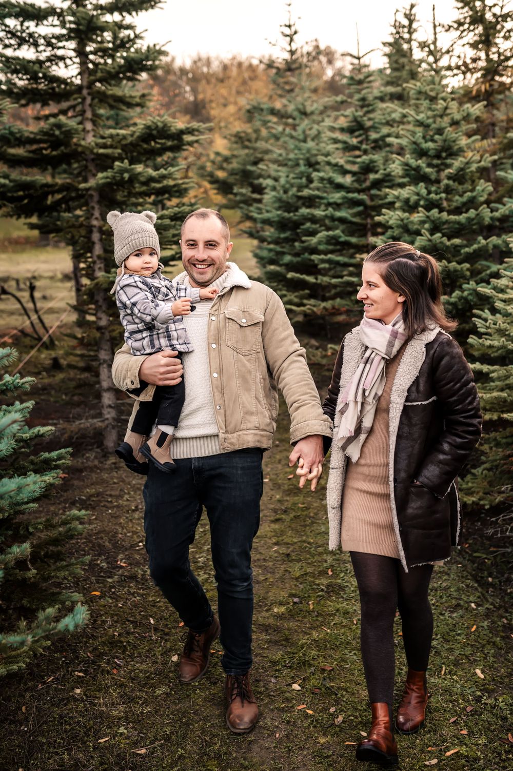A family shares a joyful moment together among evergreen trees during an autumn photoshoot.