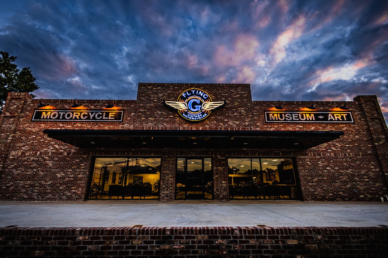 Motorcycle dealership storefront with dramatic sunset clouds.