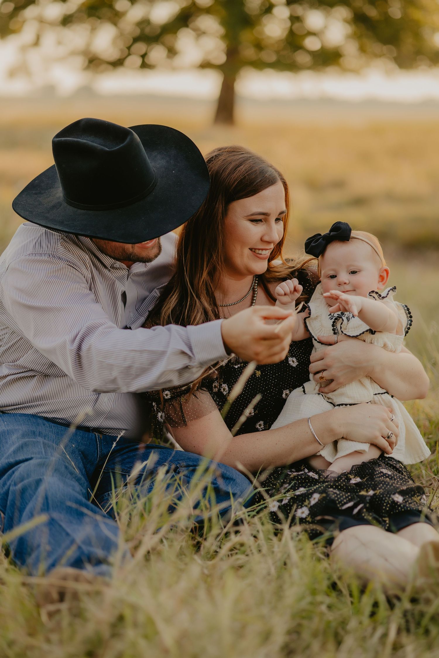 Family lying in tall grass during golden hour outdoor photo session.