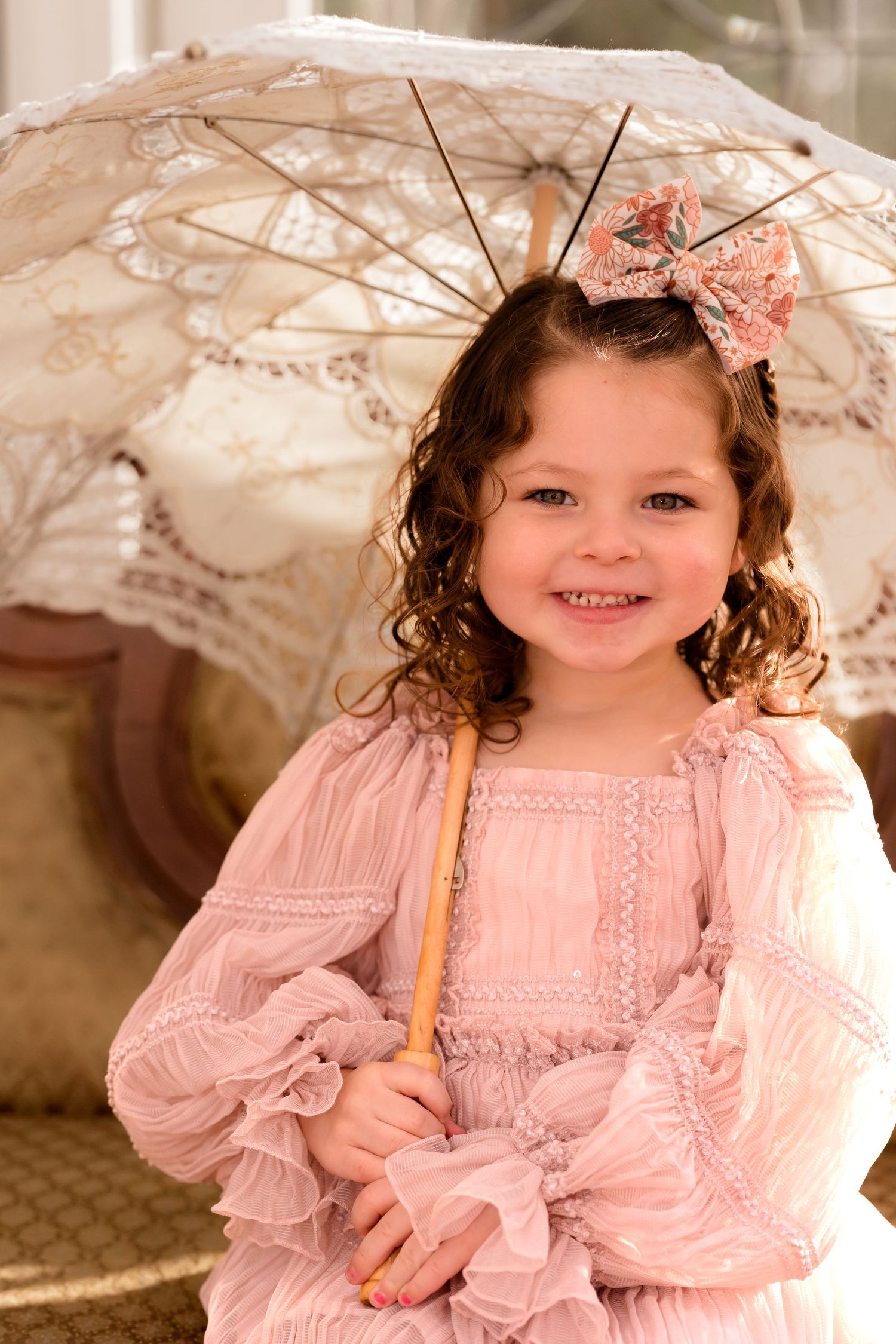 A child in a pink dress poses with a vintage lace parasol against a light background.