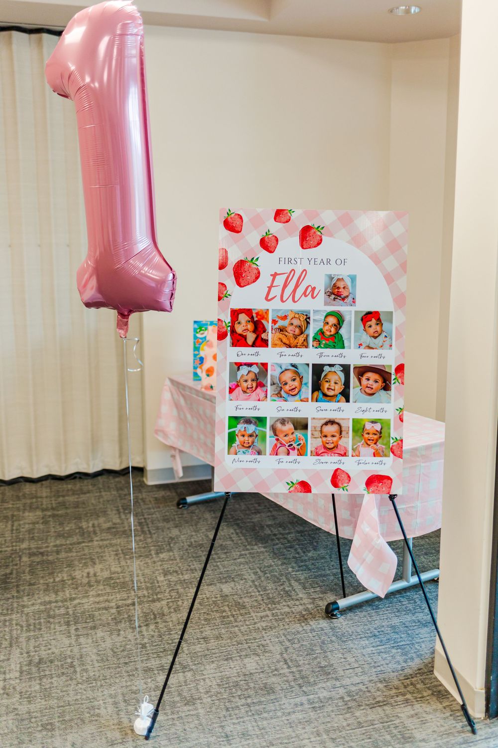 Pink number one balloon and strawberry-themed display board at a birthday party.