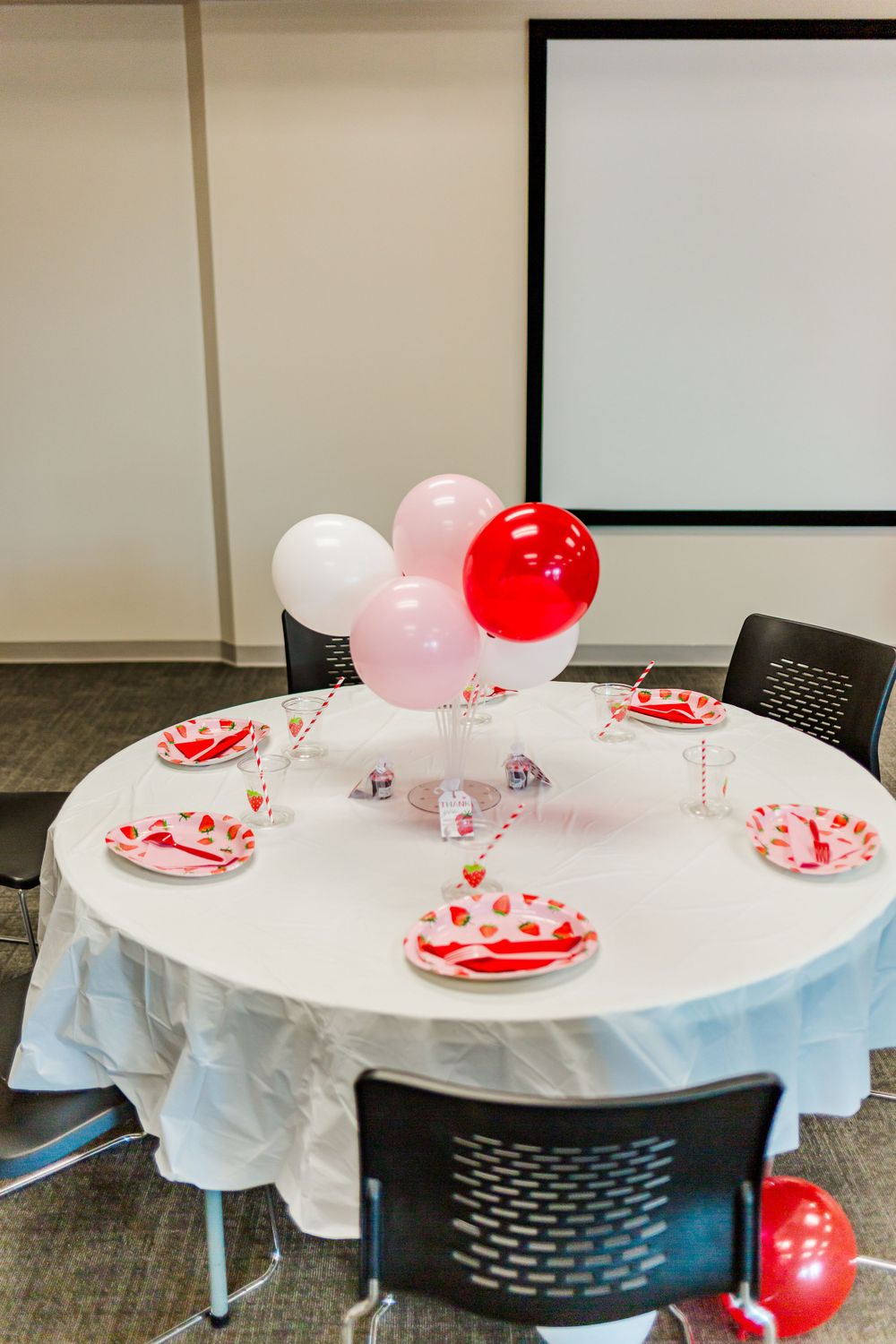 Round table decorated with pink and red balloons and strawberry-themed party plates.