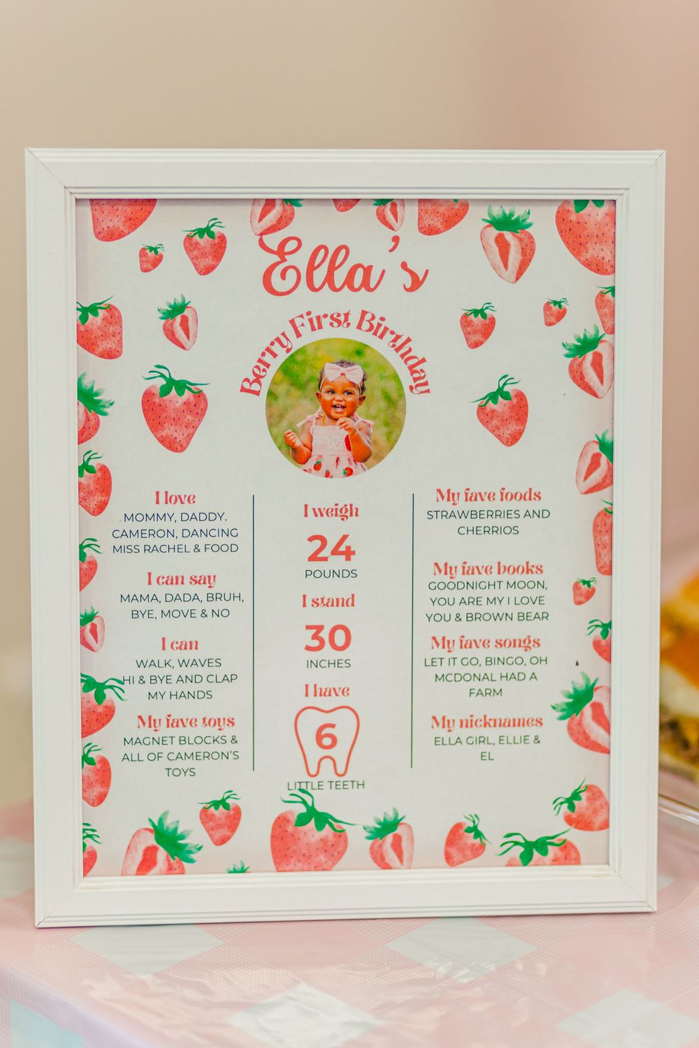 Framed first birthday milestone board with strawberry theme design and personal stats.