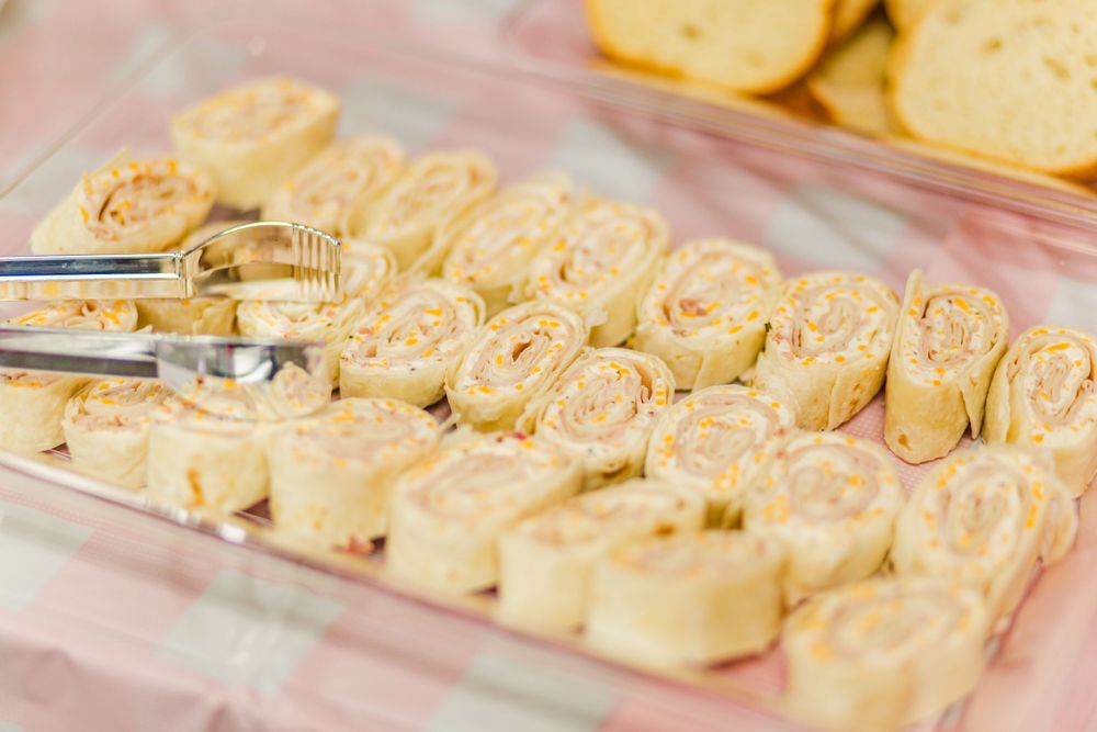 Row of sliced pinwheel sandwiches arranged on a clear serving tray.