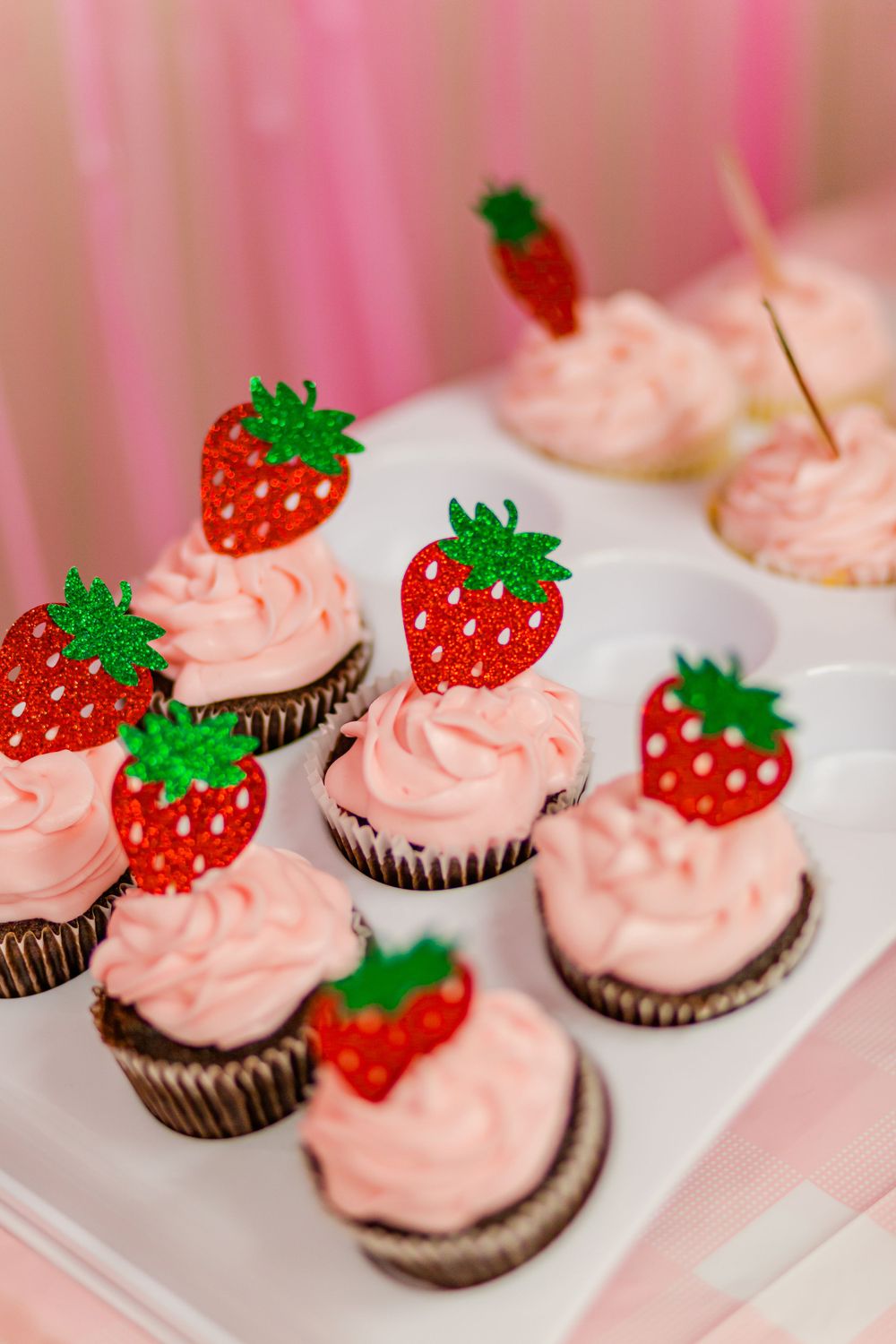 Chocolate cupcakes topped with pink frosting and strawberry decorations.
