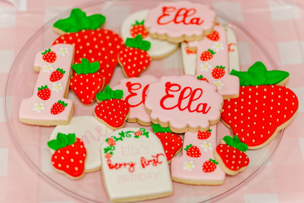 Decorated sugar cookies with strawberry designs and pink text on a white plate.