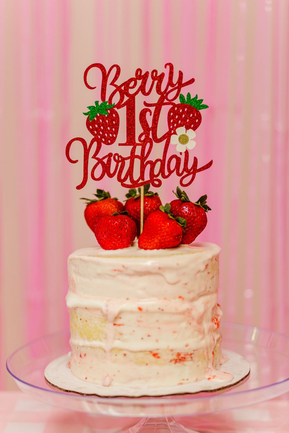 White birthday cake with strawberry decorations and a red 'Berry 1st Birthday' cake topper.