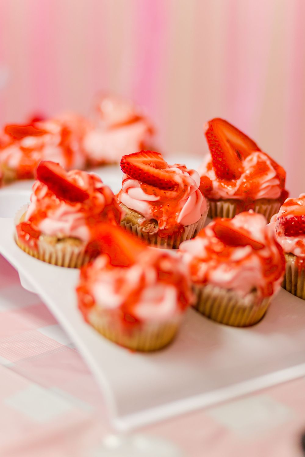 Cupcakes topped with pink frosting and fresh strawberry slices on a white platter.