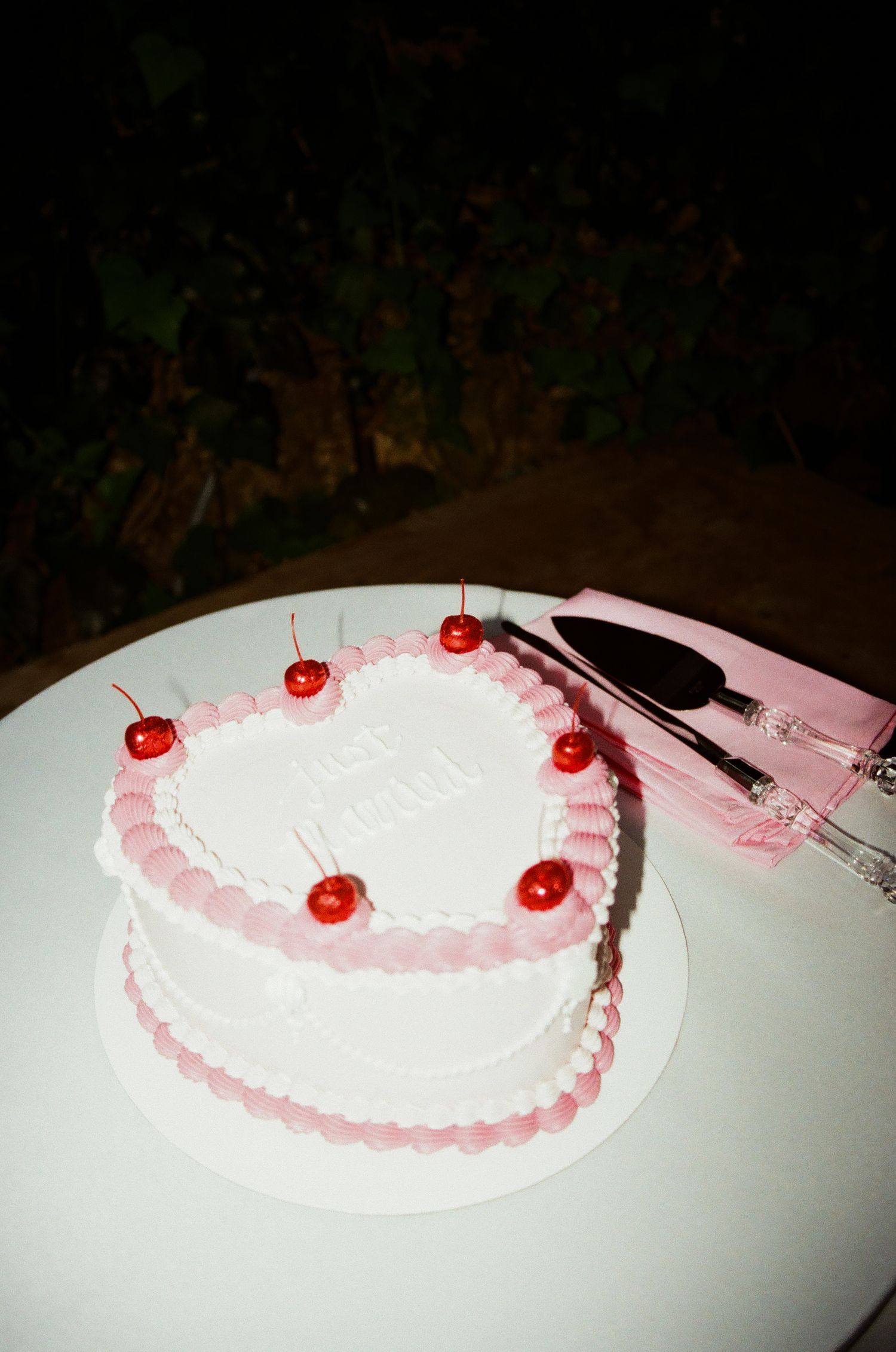 A white wedding cake decorated with pink frosting and maraschino cherries.
