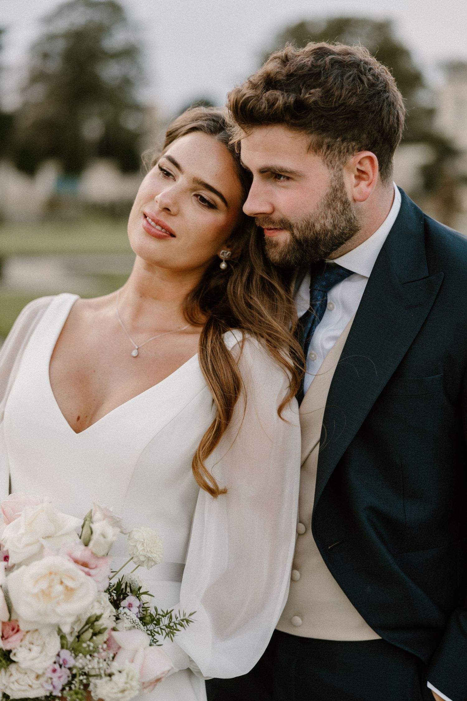 A romantic wedding portrait showcasing elegant bridal attire and formal wear in an outdoor garden setting.
