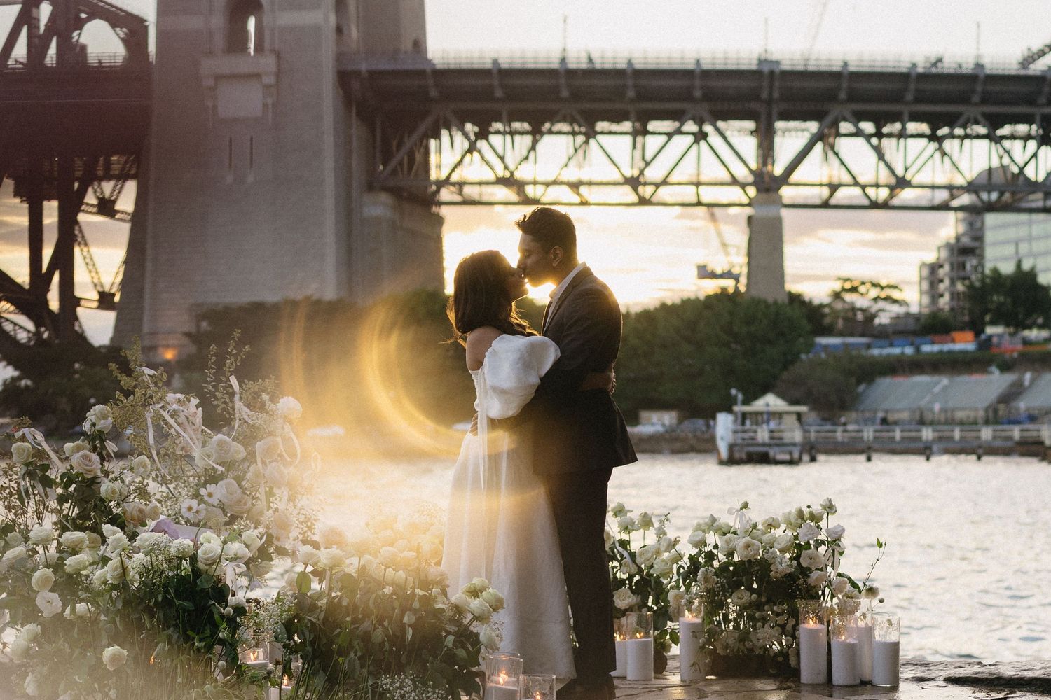 A couple stands in silhouette against the Manhattan skyline across the water.