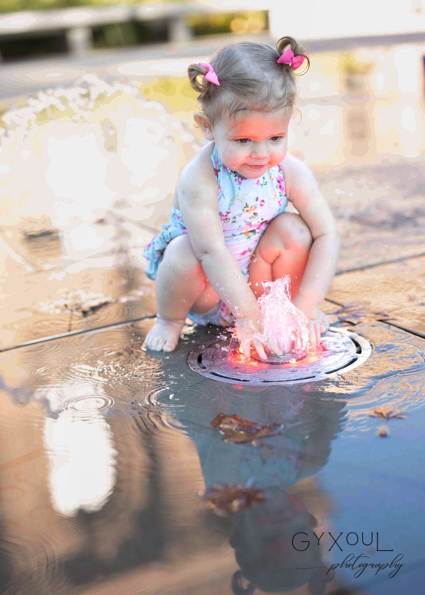 Child in floral swimsuit splashing in water fountain on sunny day.