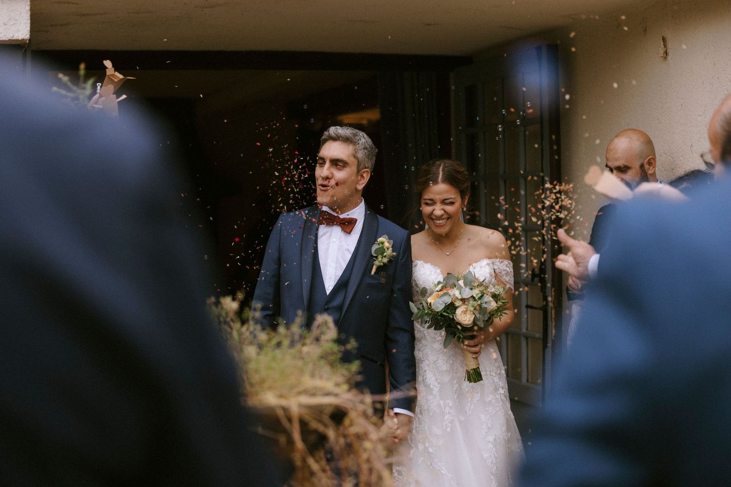 A newlywed couple exits their wedding ceremony amid falling confetti and guests.