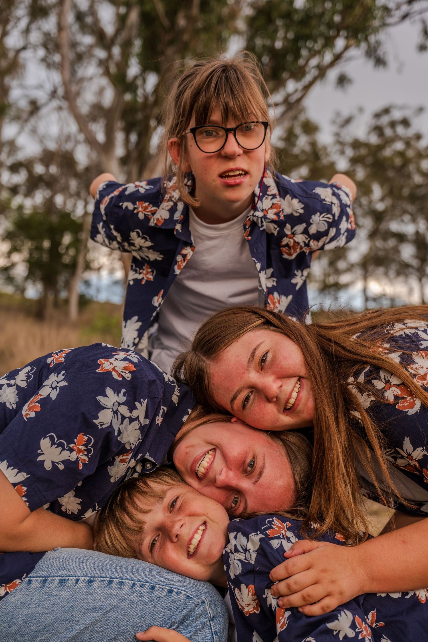 A playful group stacks on top of each other wearing matching floral shirts outdoors.
