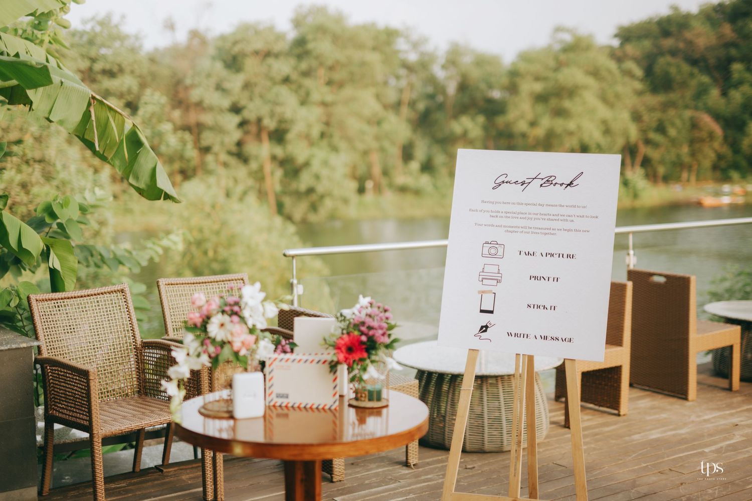 Outdoor wedding reception setup with rattan furniture, floral arrangements, and a menu sign on an easel.