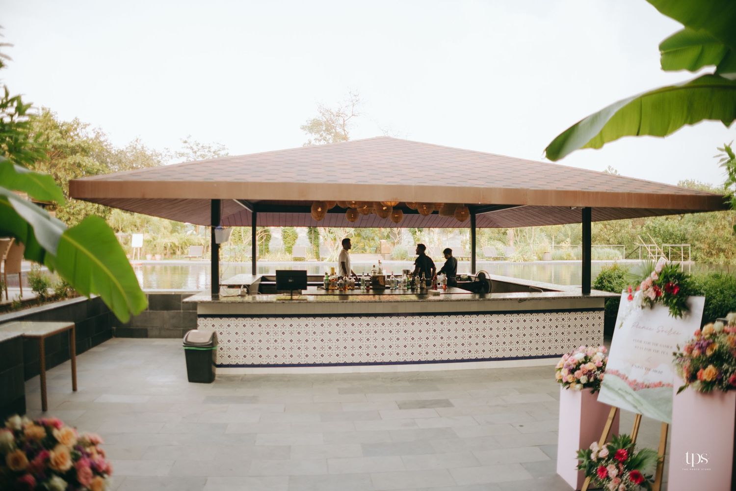 Covered outdoor bar area decorated with flowers and surrounded by tropical landscaping.