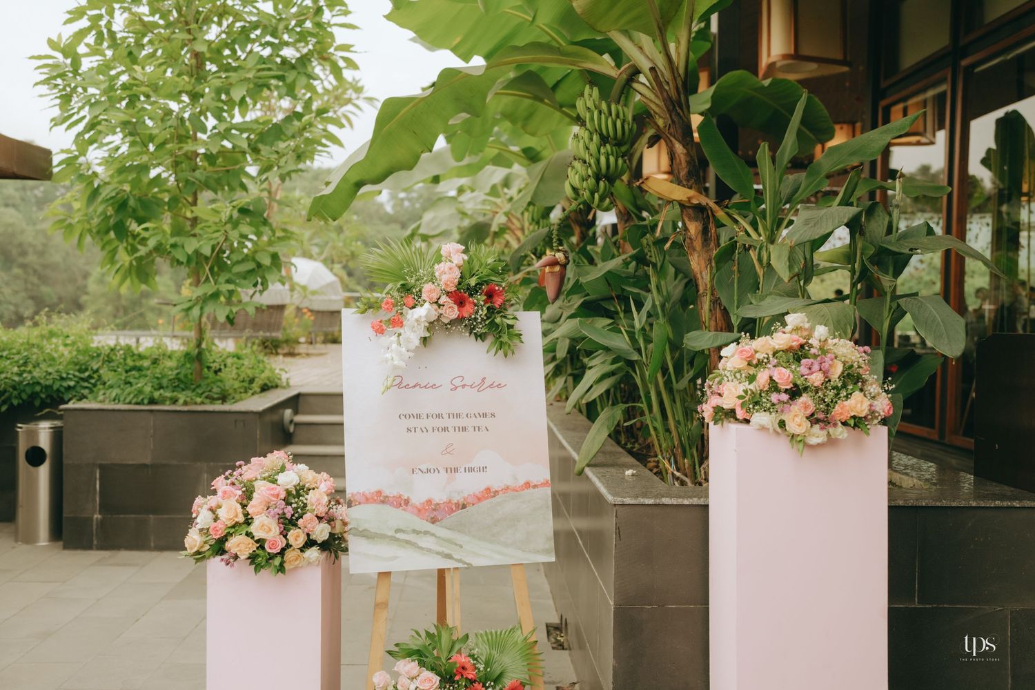 Wedding welcome sign surrounded by pink floral arrangements and tropical greenery.