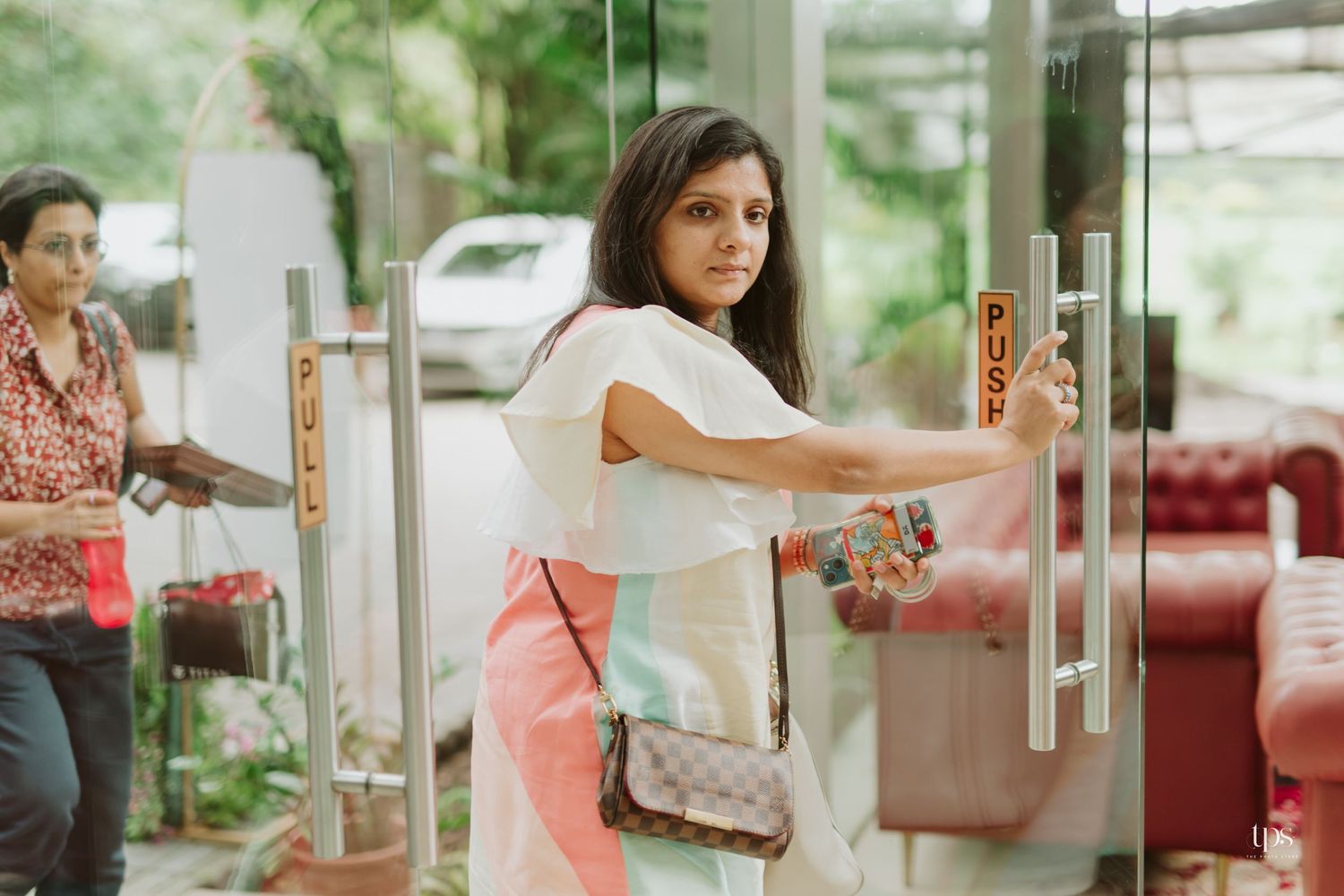 Woman in white top and pink skirt opening a glass door.