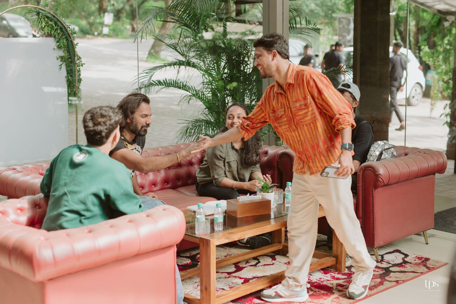 Guests seated on red couches in an outdoor covered patio area with lush greenery in the background.